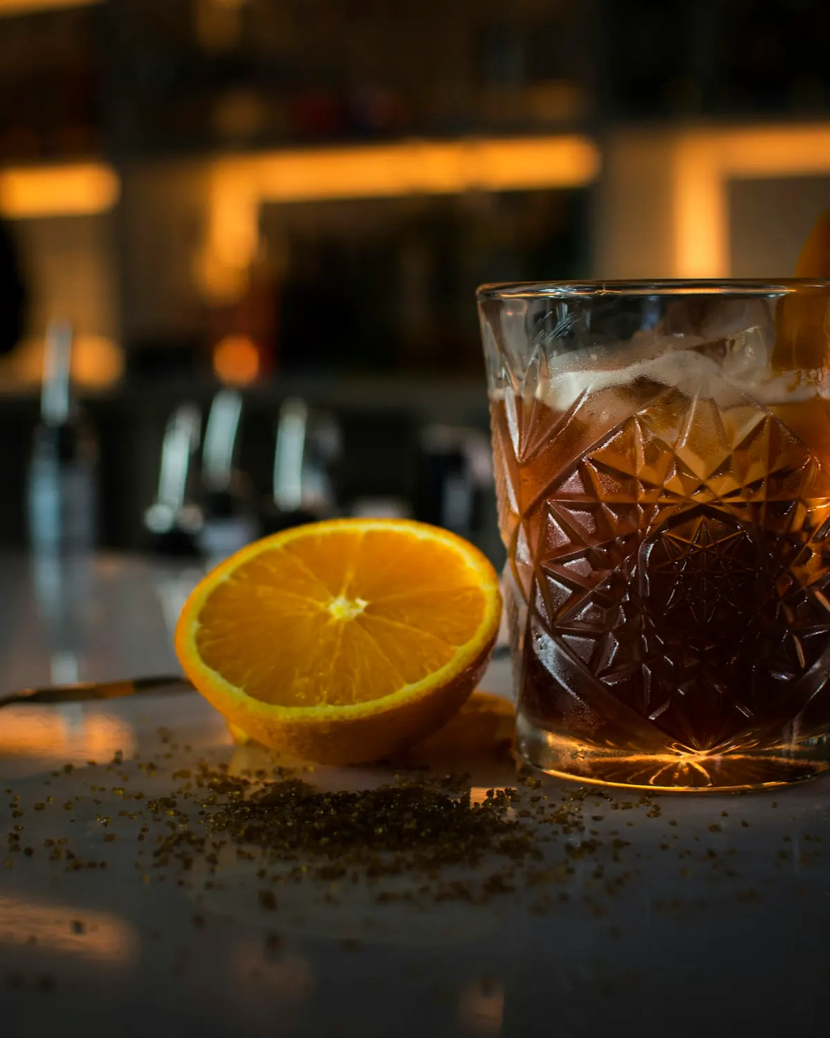 Míchaný drink v broušené sklenici a půlka pomeranče na barovém pultu